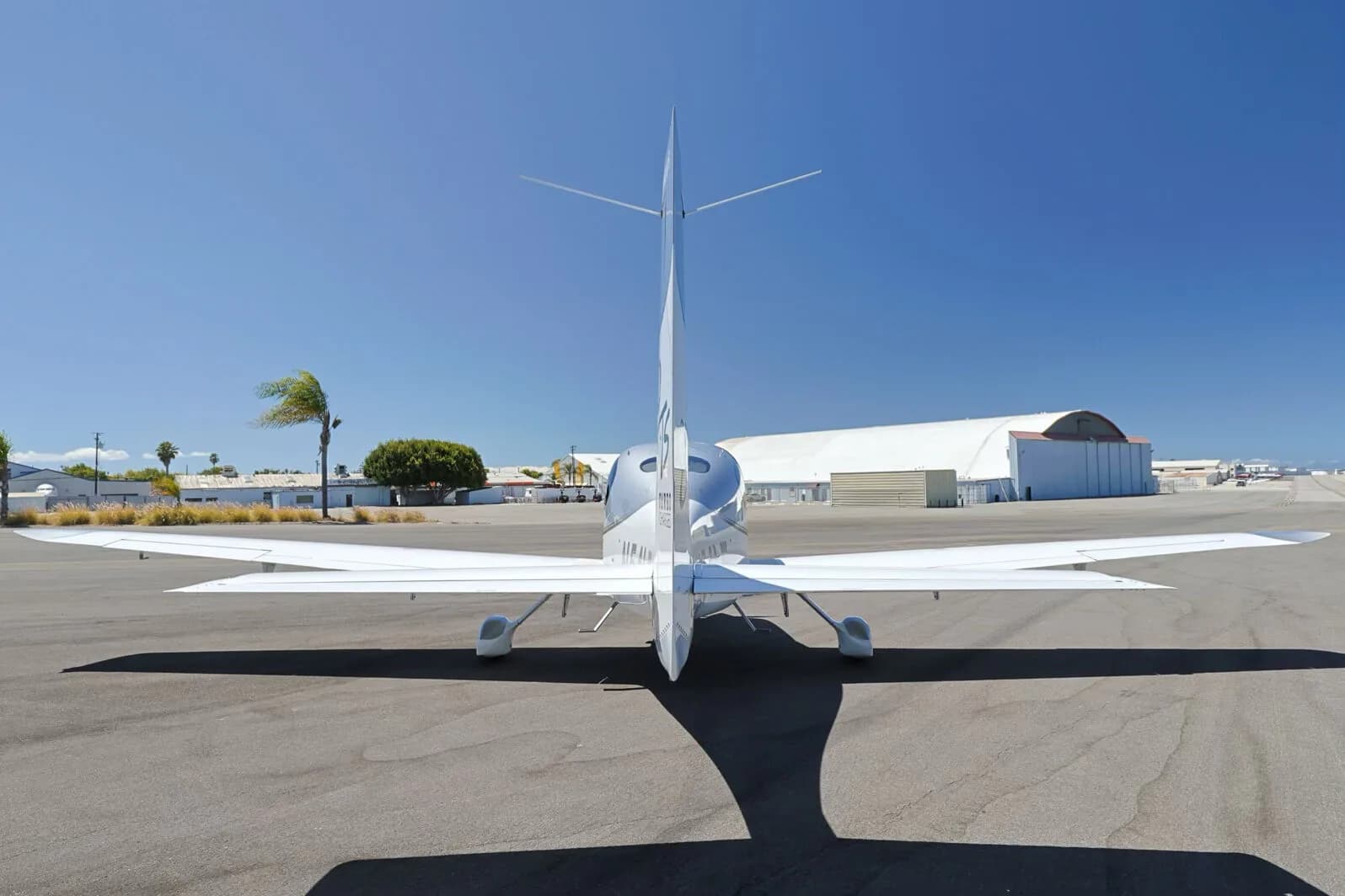 Rear view of a silver and white Cirrus SR22T (N54LW) on an tarmac, with hangars in the distance.