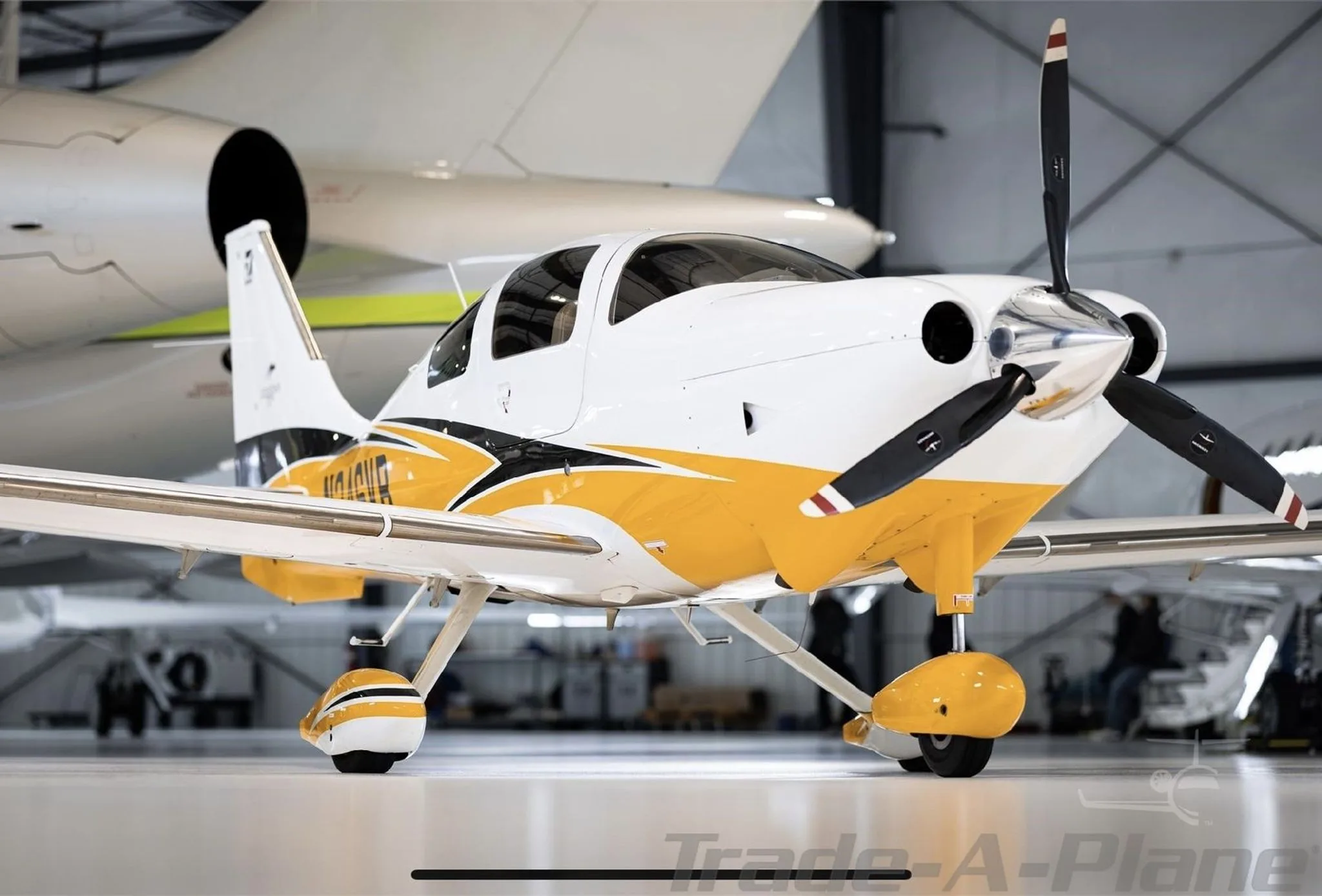 A front view of the white and yellow Cessna TTx aircraft N246VB with a propeller, parked in a hangar.