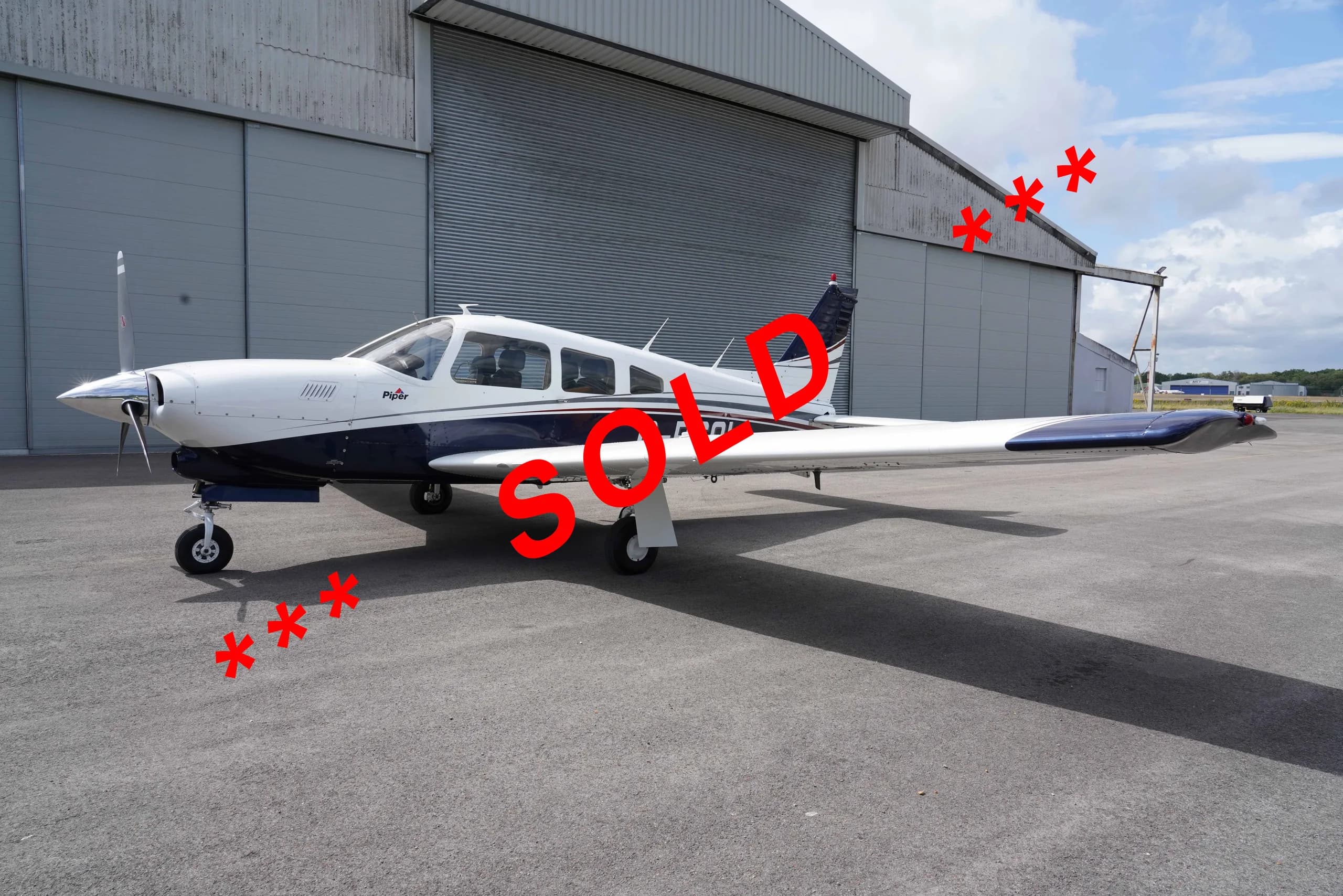 A white and blue Piper single-engine aircraft is parked on a tarmac in front of a hangar.