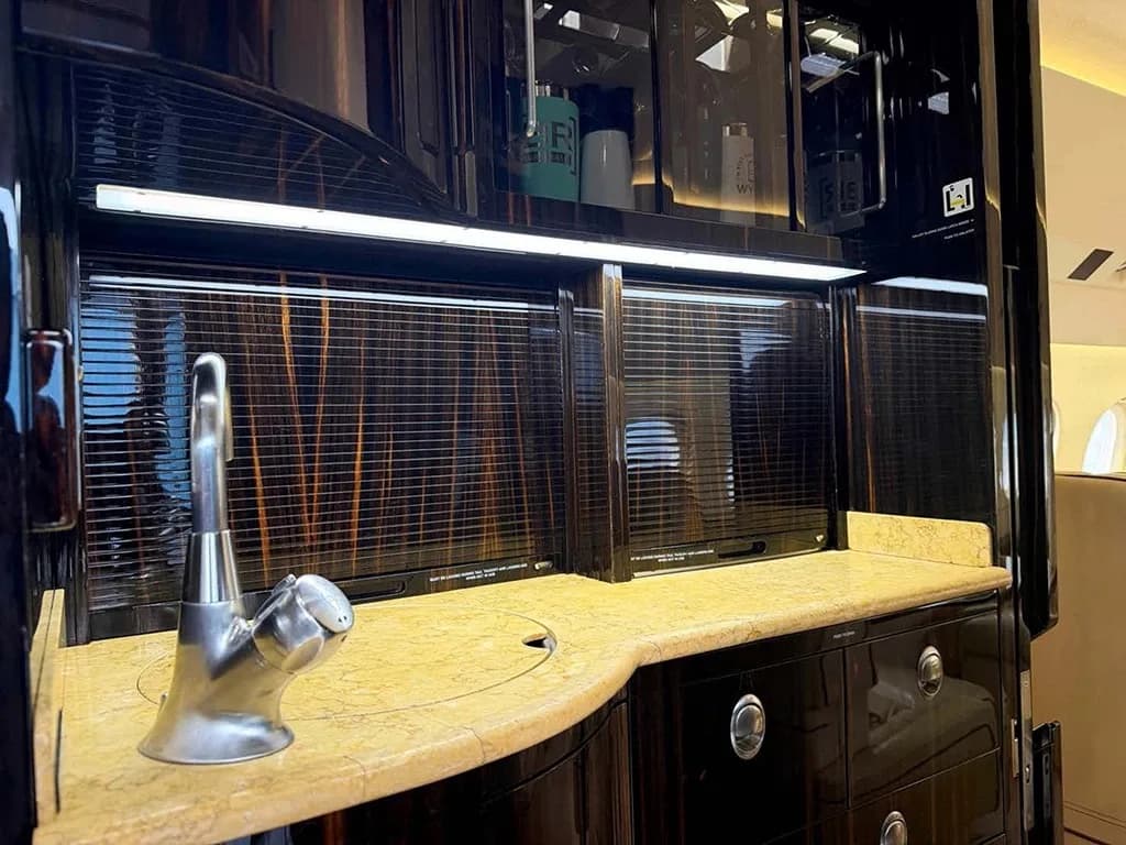 A luxurious aircraft galley with dark wood cabinetry, a light-colored countertop, and a chrome faucet.