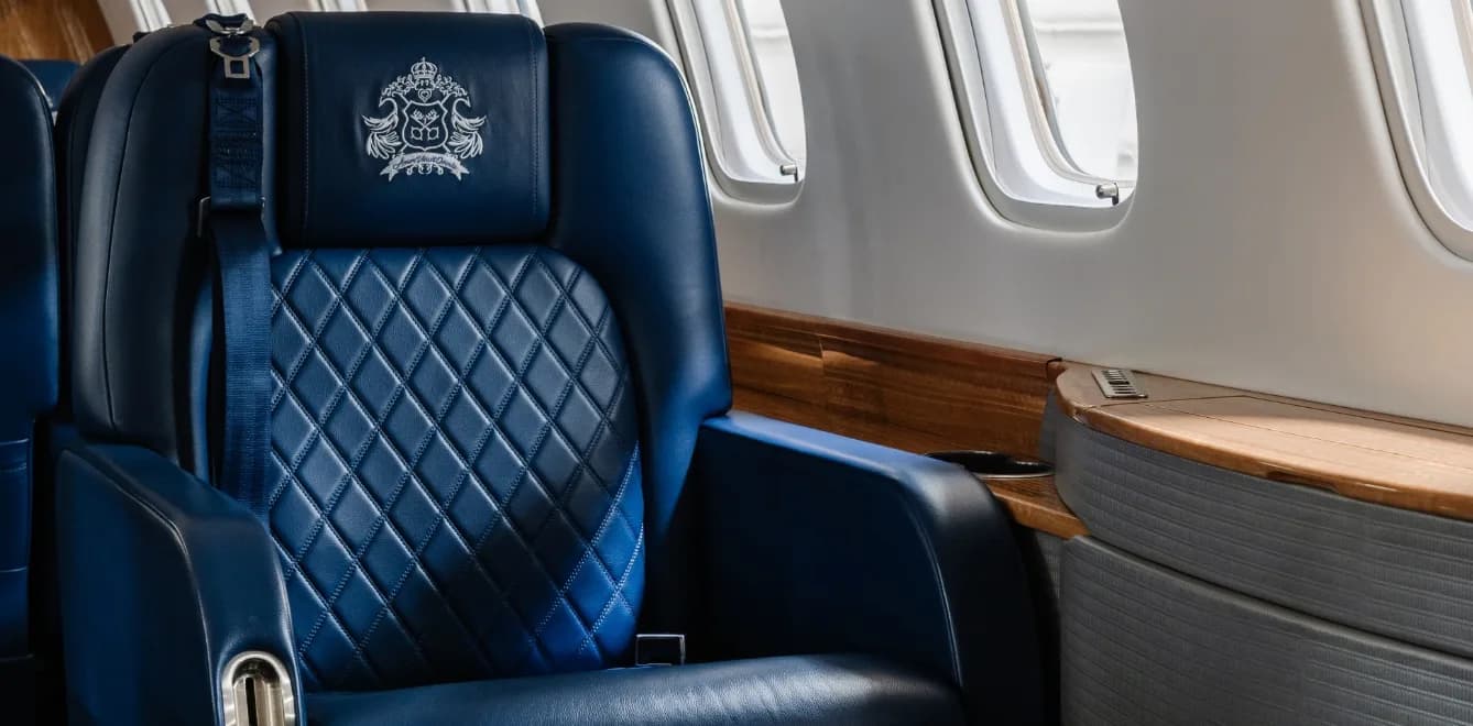 Close-up of a blue leather aircraft seat with a custom crest design on the headrest.