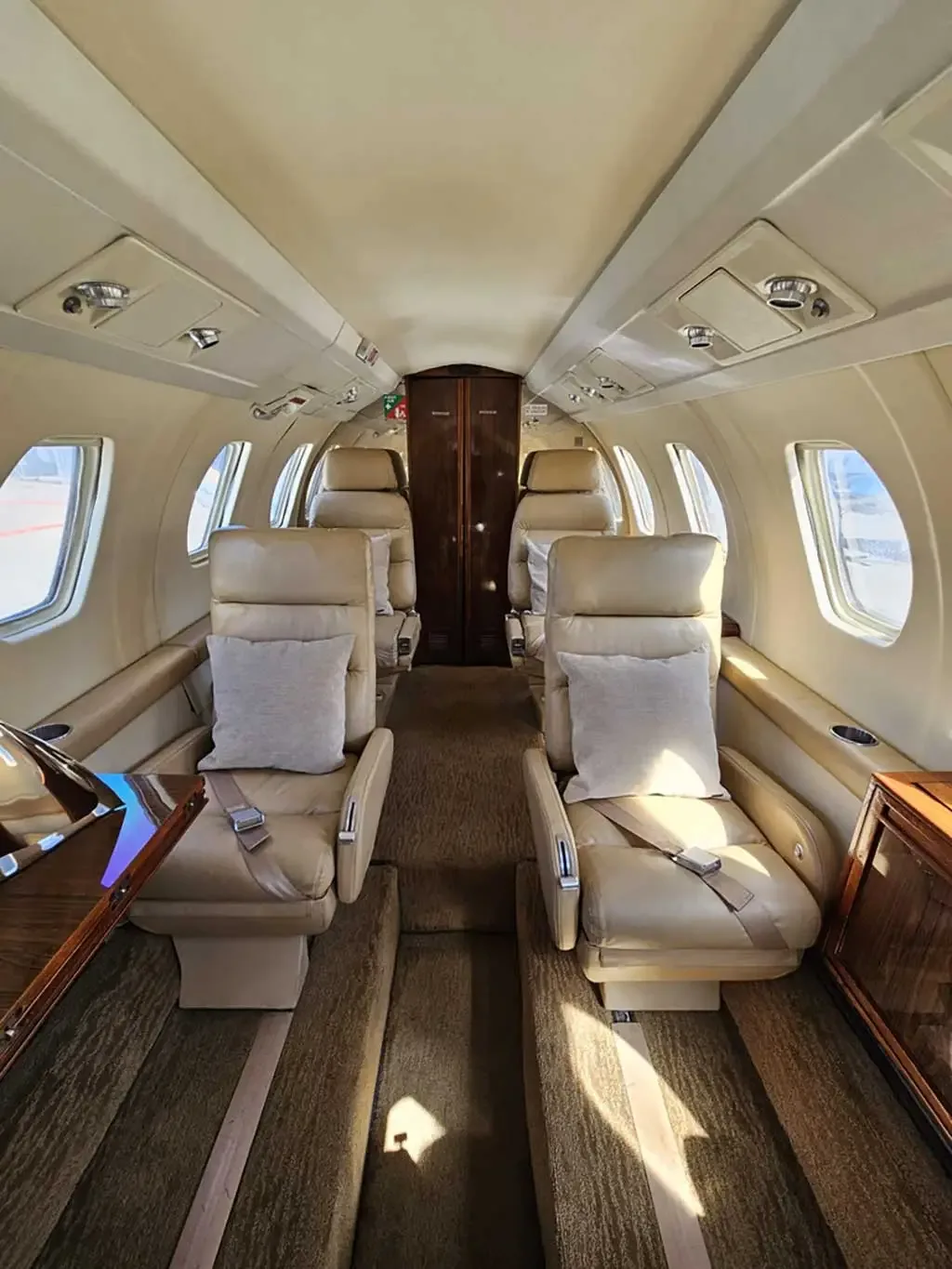 The interior cabin of a private jet with tan leather seats and a central aisle.