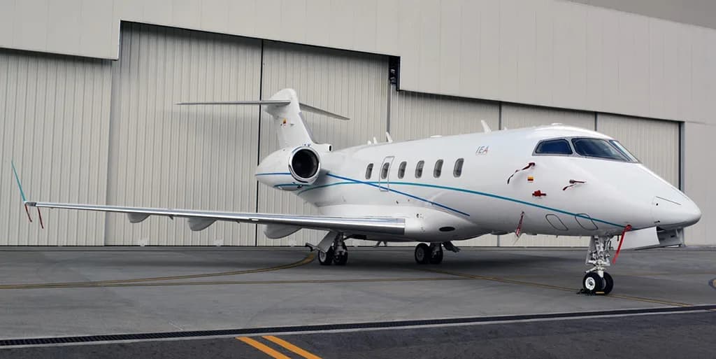 A white business jet with blue and teal stripes, registration "IEA", is parked on a tarmac in front of a closed hangar door.