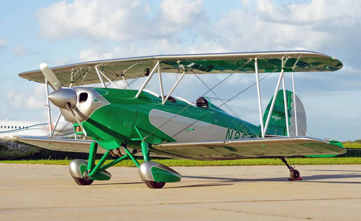 The green and silver biplane is parked on the tarmac with a cloudy sky overhead.