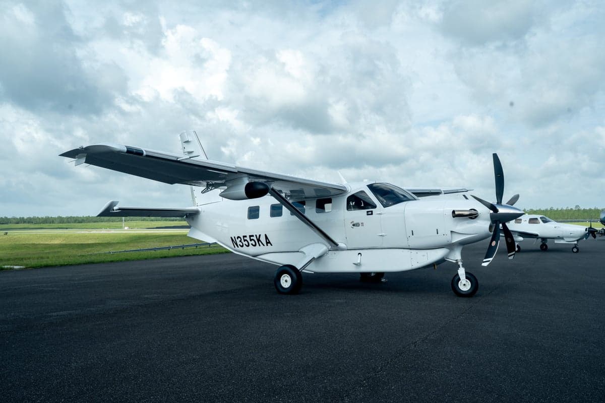 A white Quest Kodiak 100 aircraft, registration N355KA, parked on an airfield with another aircraft in the background.