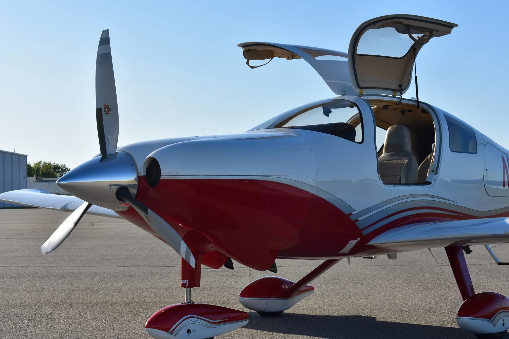 A three-quarter front view of the white and red Cirrus SR22 aircraft with its gull-wing doors open, parked on an airfield.