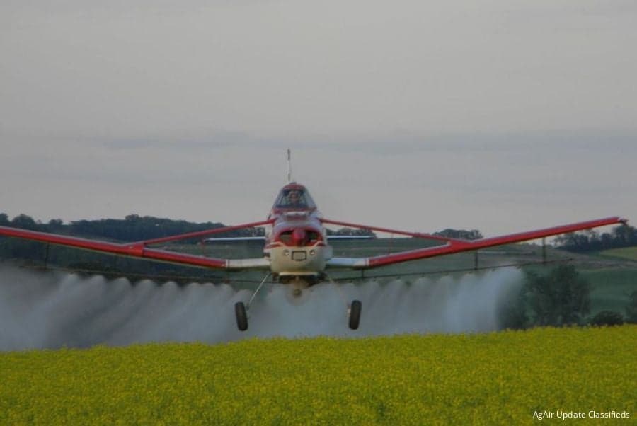 Red and white Air Tractor crop duster spraying a field of yellow flowers.