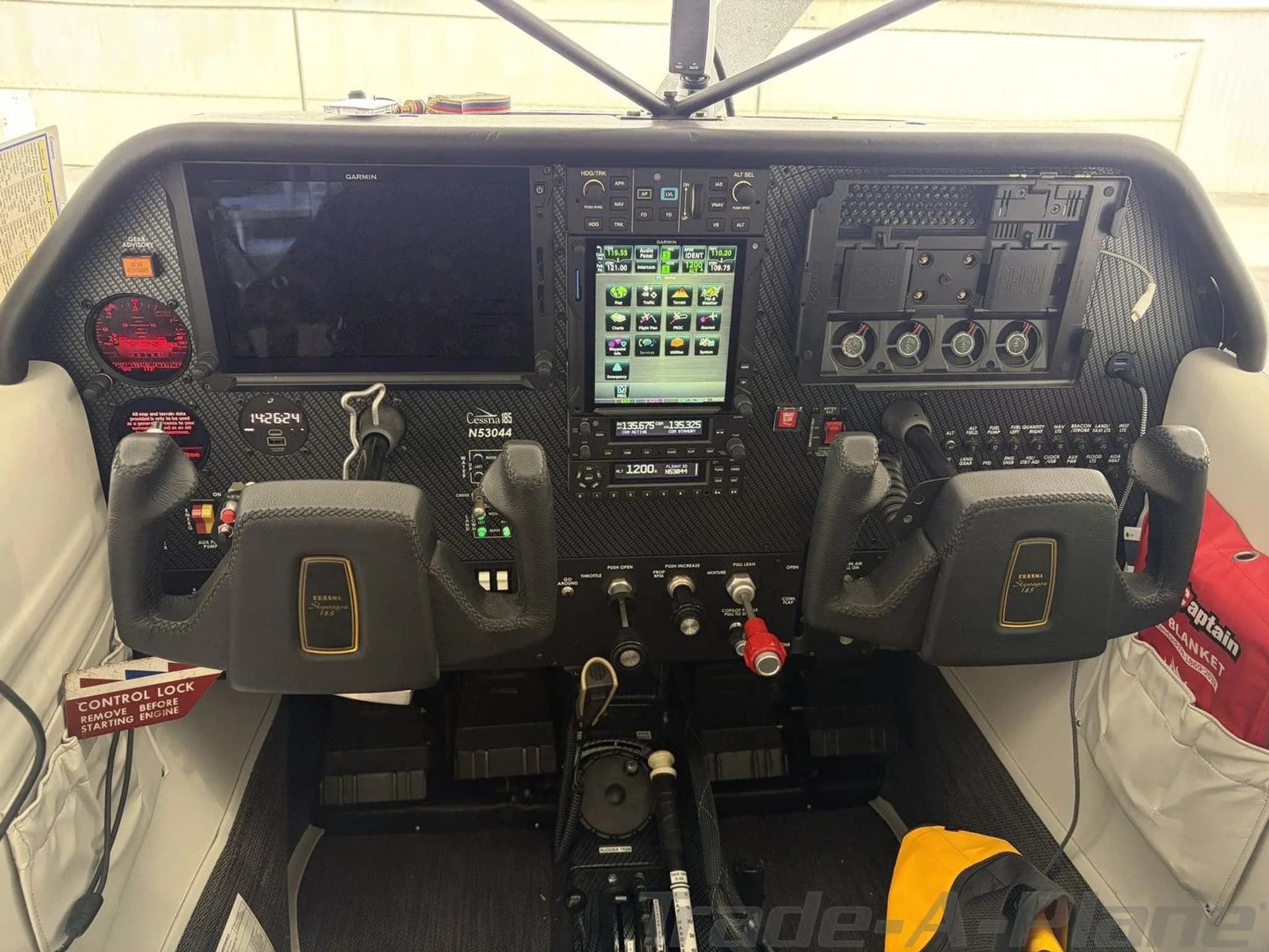 A detailed view of the Cessna 180 Skywagon's cockpit, showing the Garmin avionics suite and control yokes.