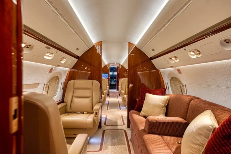 A view down the luxurious cabin of a business jet, showing tan leather seats and a brown sofa.