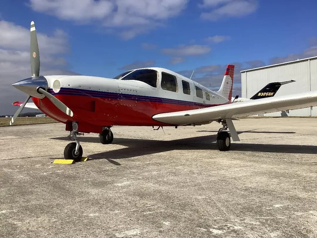 A red and white single-engine propeller aircraft, N3258H, parked on an airfield under a partly cloudy sky.