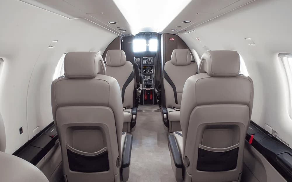 The interior cabin of a Pilatus PC-12 aircraft, looking forward from the rear seats towards the cockpit.
