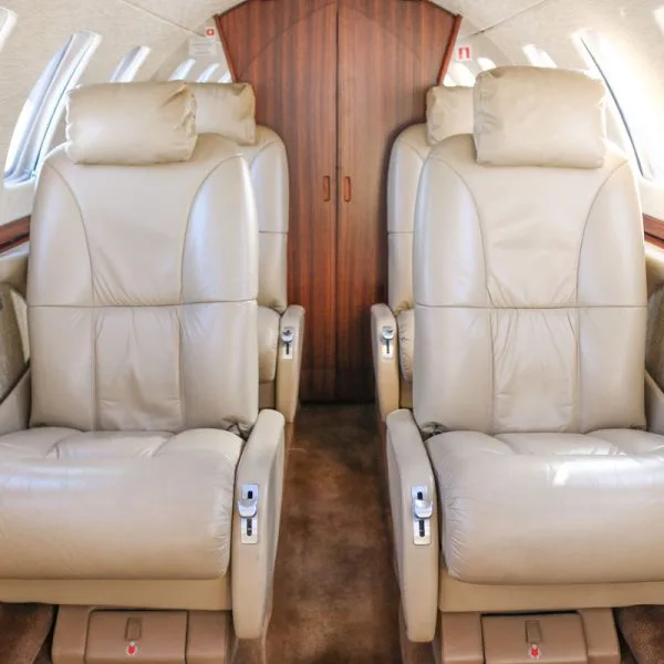 Interior view of an aircraft cabin with two rows of beige leather seats facing each other.