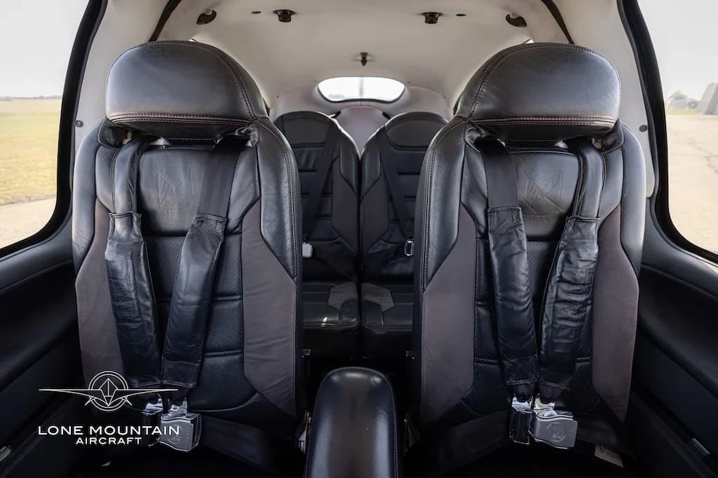The black leather front and rear passenger seats of an aircraft cabin, viewed from the back.