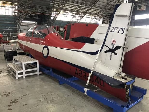 Rear side view of a red and white Pilatus PC-9 aircraft in a hangar.