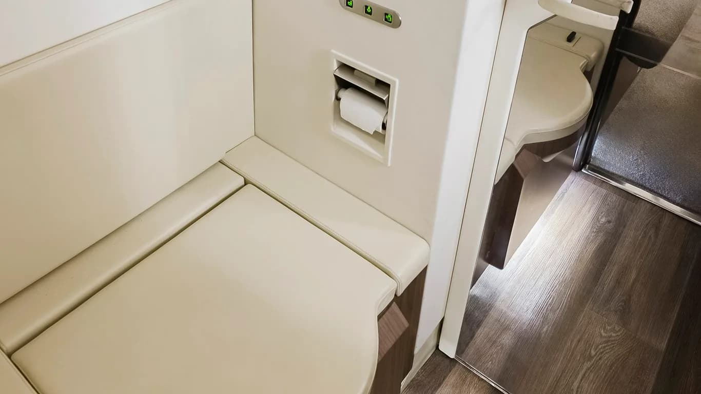 A clean aircraft lavatory with a beige toilet and a roll of toilet paper.