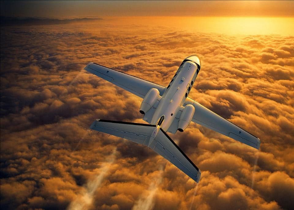 An aircraft flying above the clouds at sunset.