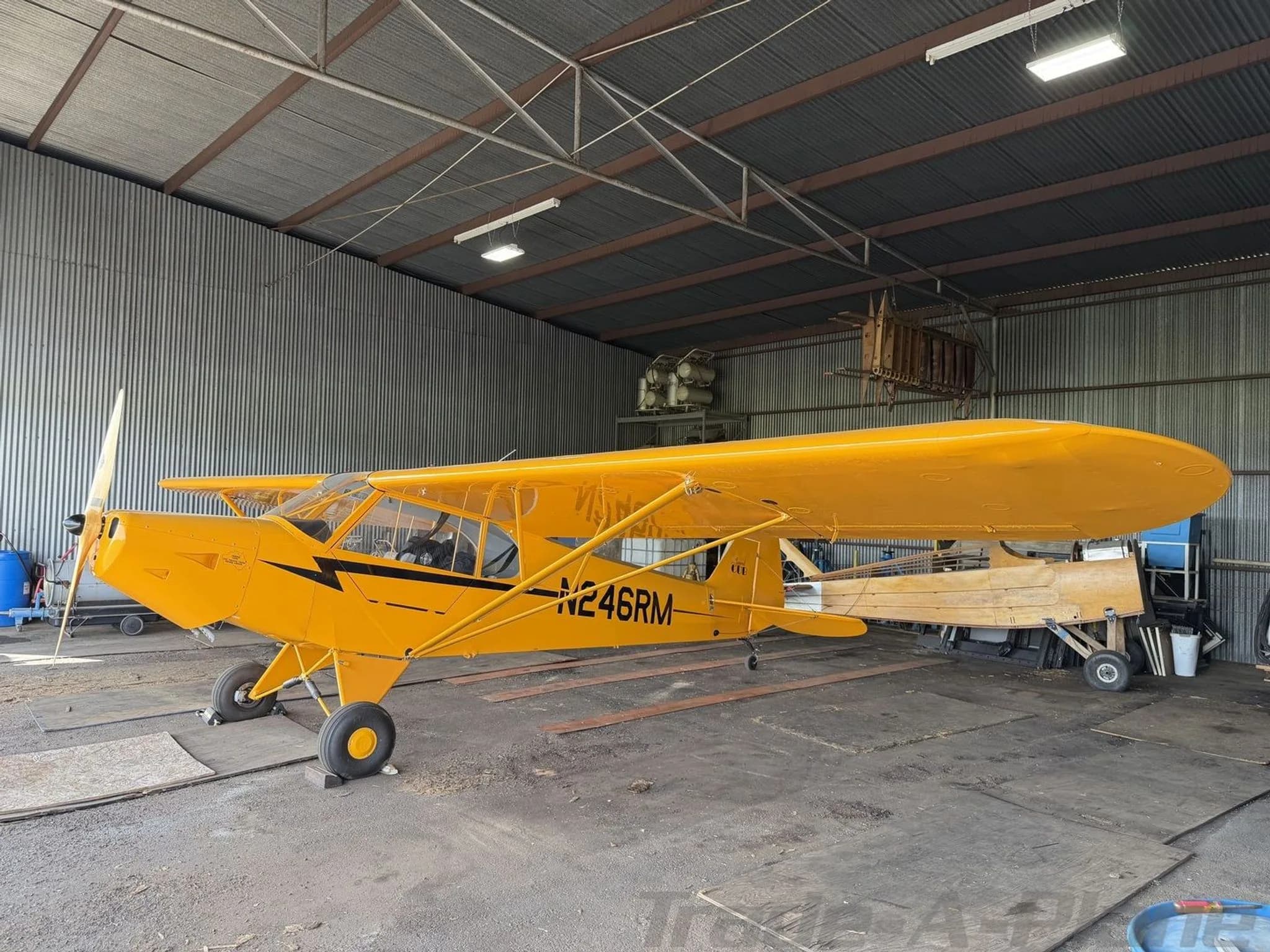 Side view of a yellow American Legend Cub aircraft with registration N246RM in a hangar.