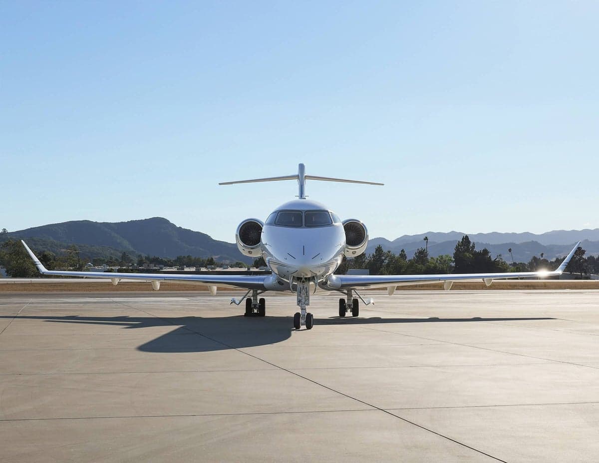 Front view of a white aircraft parked on the tarmac with mountains in the background.
