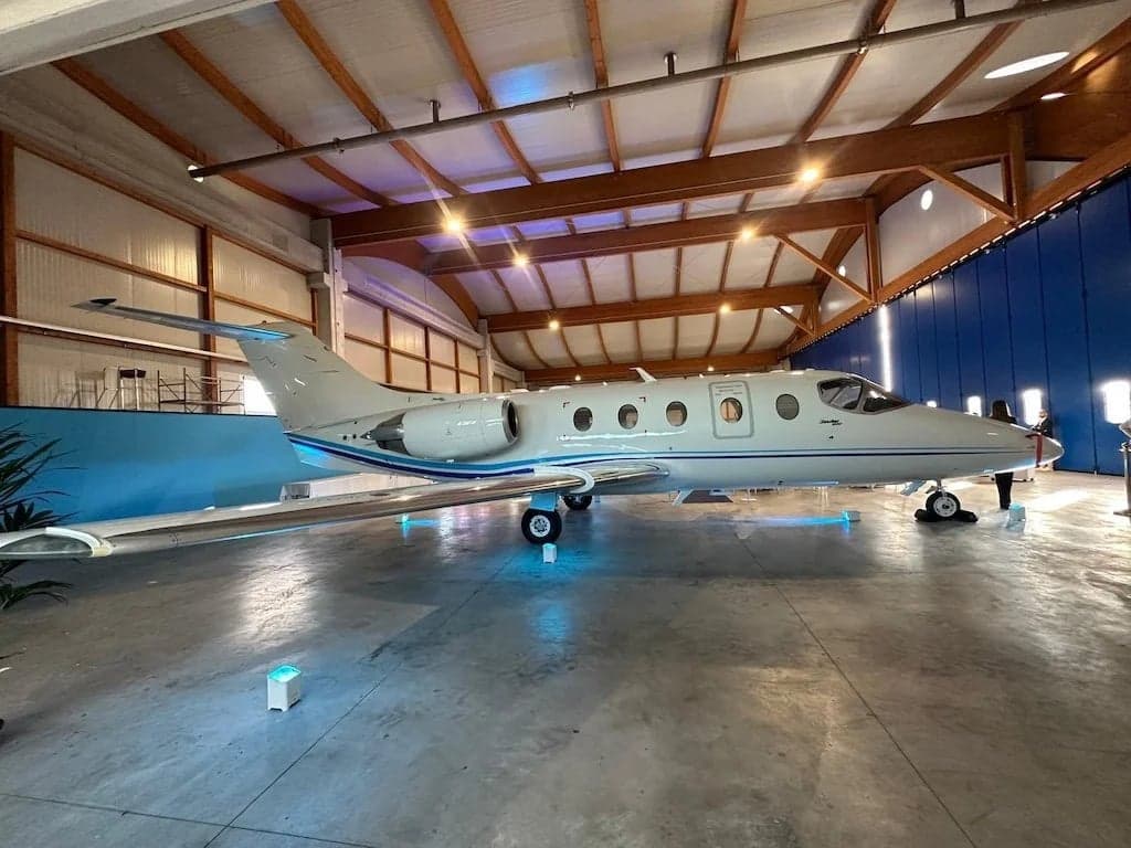 A white Learjet aircraft is parked inside a hangar with wooden beams.