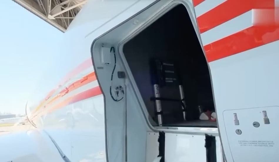 A close-up view of an open baggage compartment on the side of a white business jet with red stripes.