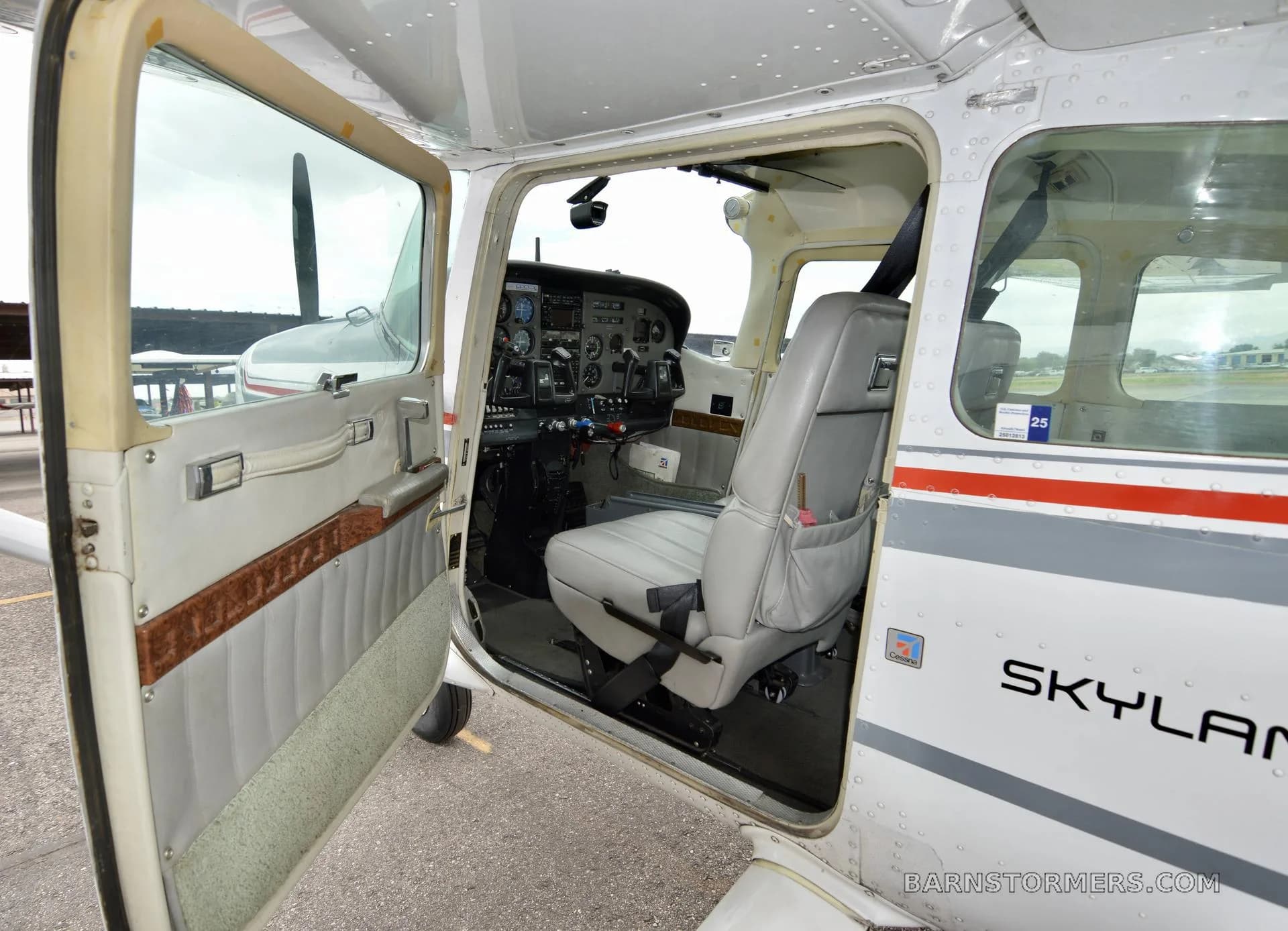 The open door of a white Cessna 182 Skylane, revealing a gray pilot's seat and the instrument panel.
