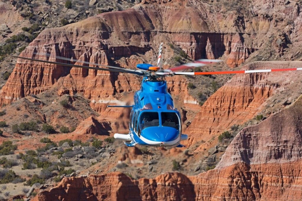A blue and white Bell 525 helicopter flying in front of a canyon landscape.