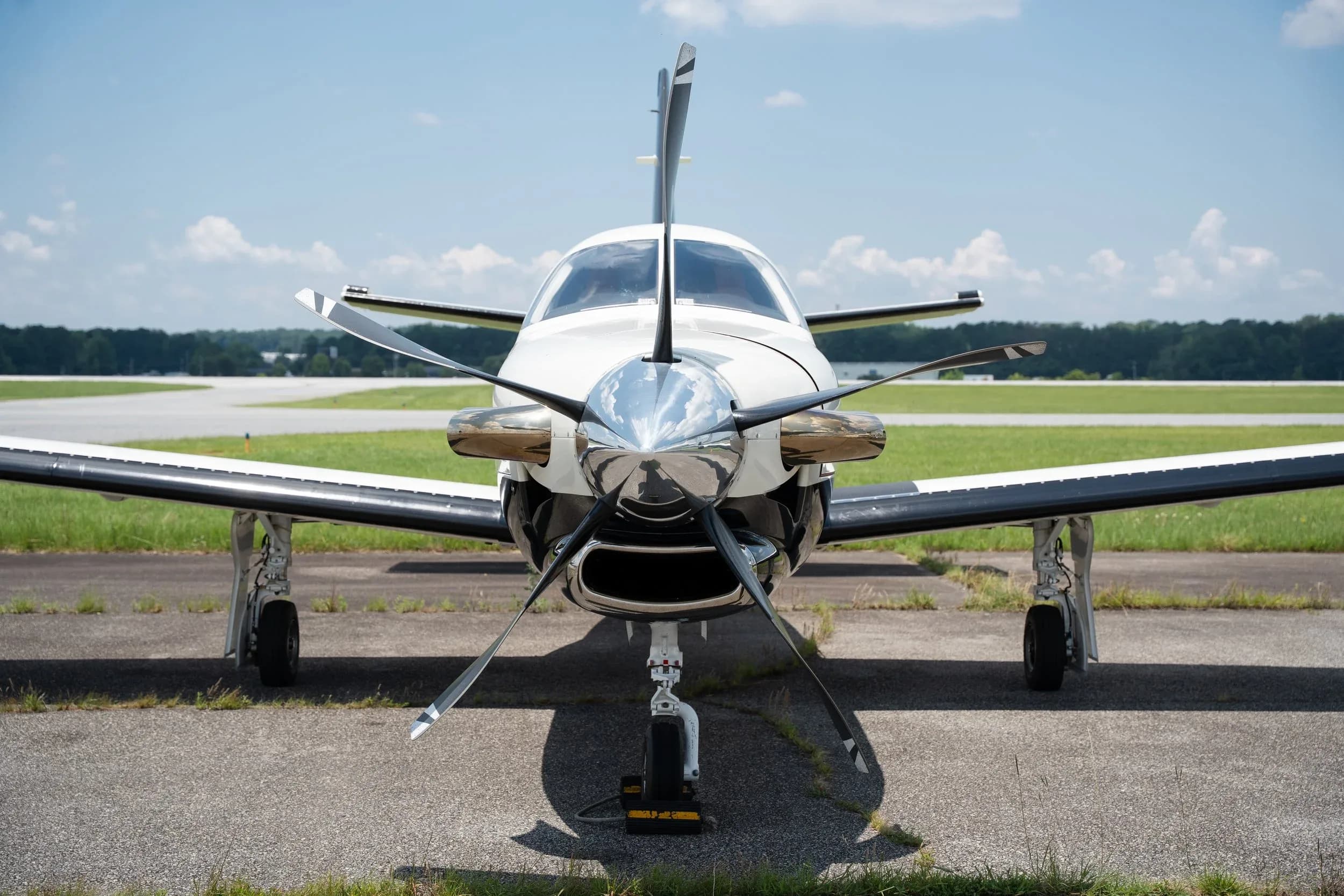A head-on view of a white and black TBM 960 aircraft with its propeller blades visible, parked on an airport tarmac.