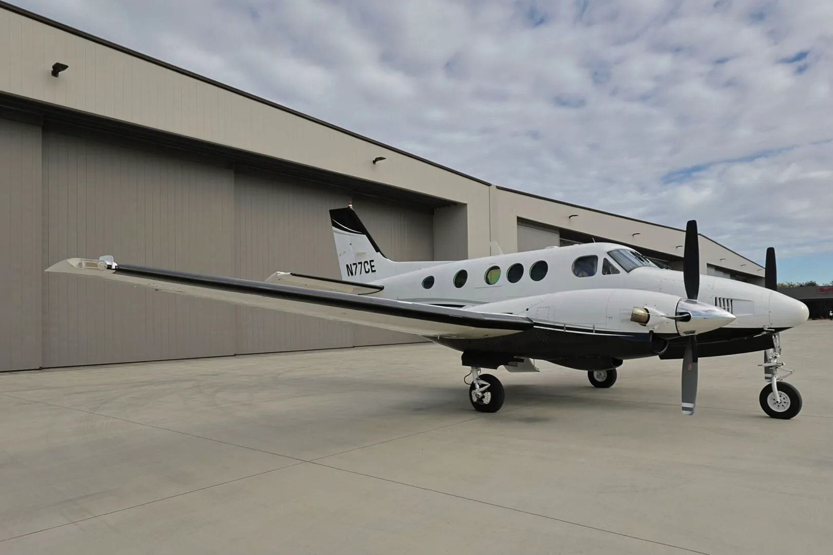 A left side view of the N77CE twin-engine turboprop aircraft with its white and black paint scheme.