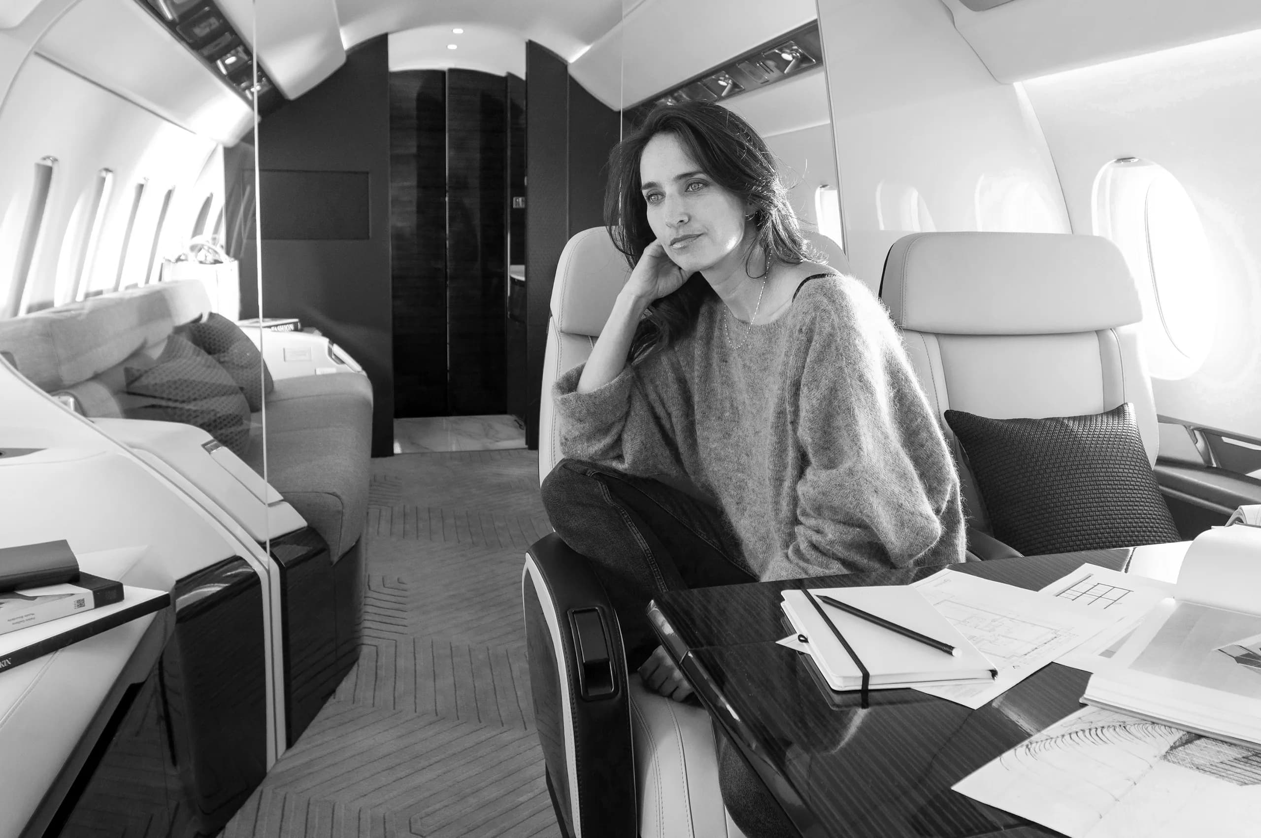 A woman sitting in a plush seat inside a private jet cabin, looking out of frame.