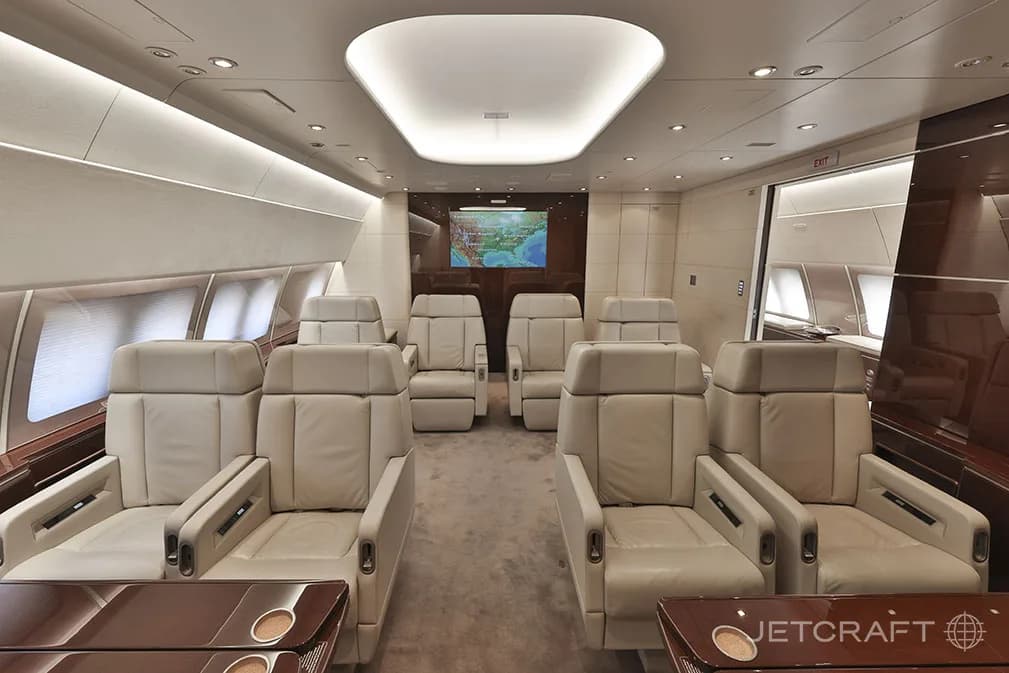 A luxurious aircraft cabin features multiple rows of cream-colored leather seats and a large screen displaying a map at the front.