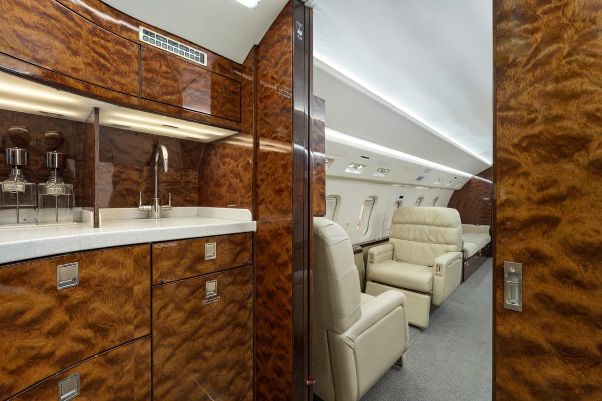 A view of the aircraft cabin with a bar area and cream-colored leather seats.