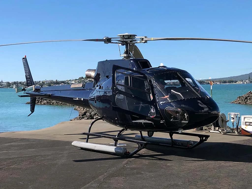 A black helicopter parked on a paved area next to a body of water.