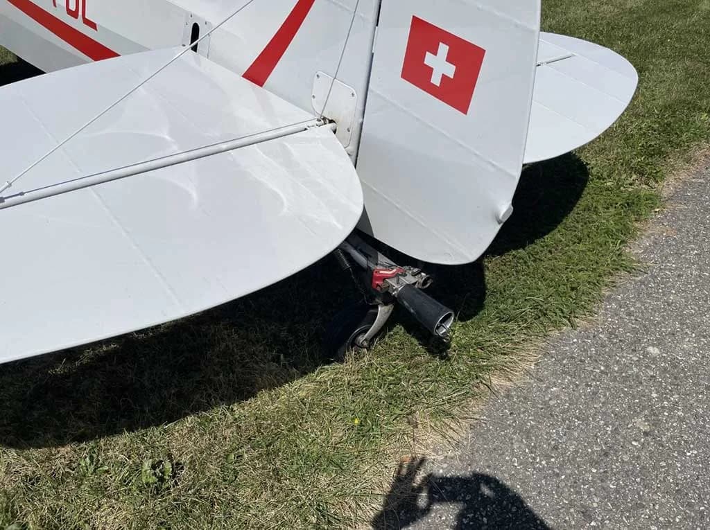 A close-up view of the tail section of a white aircraft showing the Swiss flag on the rudder and the tailwheel.