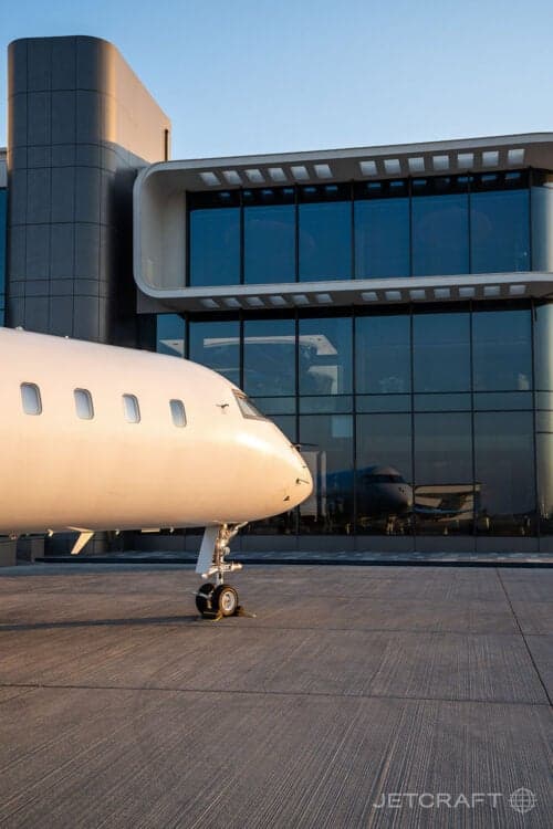Close-up of the nose of a white aircraft parked in front of a modern building.