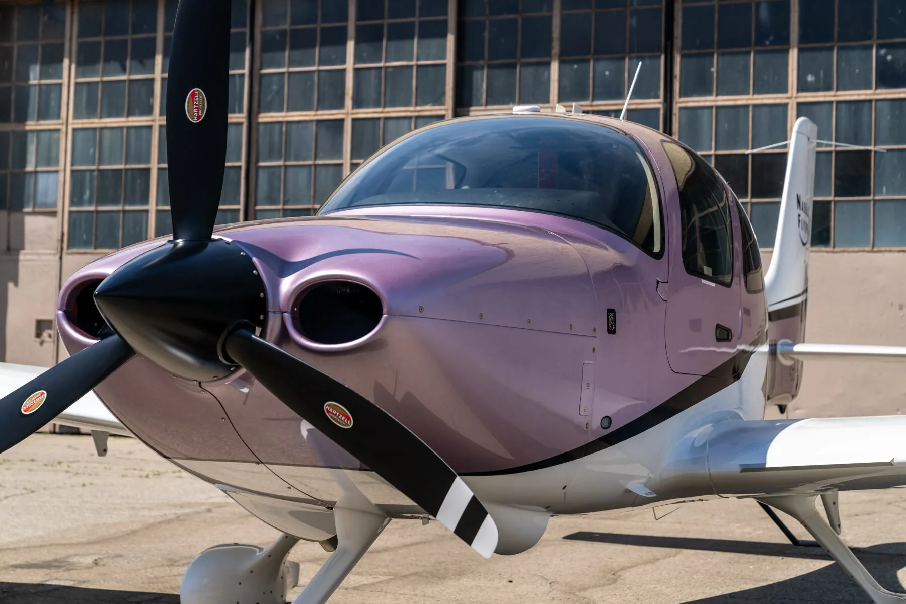 A close-up front view of the metallic lavender Cirrus SR22 aircraft, showing its propeller and nose.
