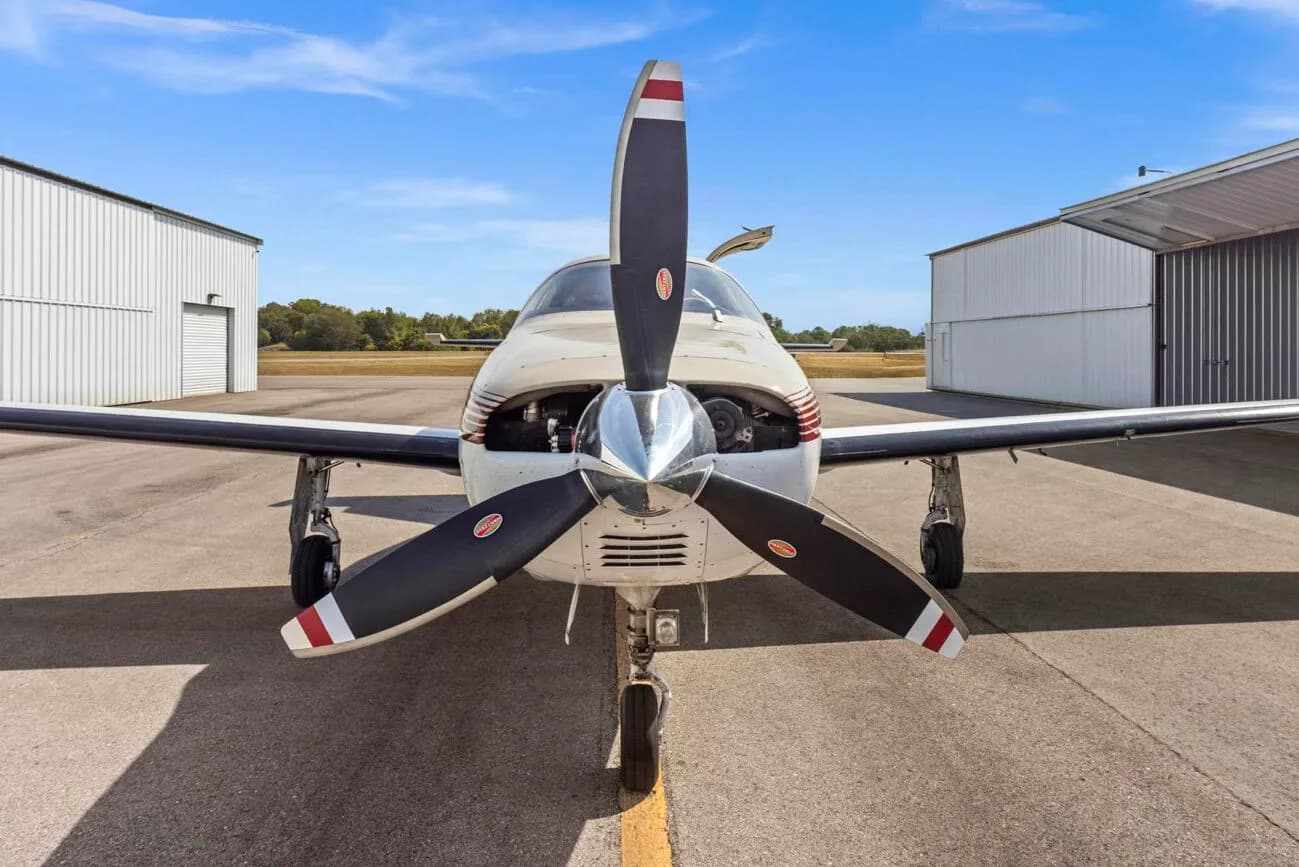 A head-on view of the Piper Malibu N31BX, showing its propeller and engine cowling, parked between two hangars.