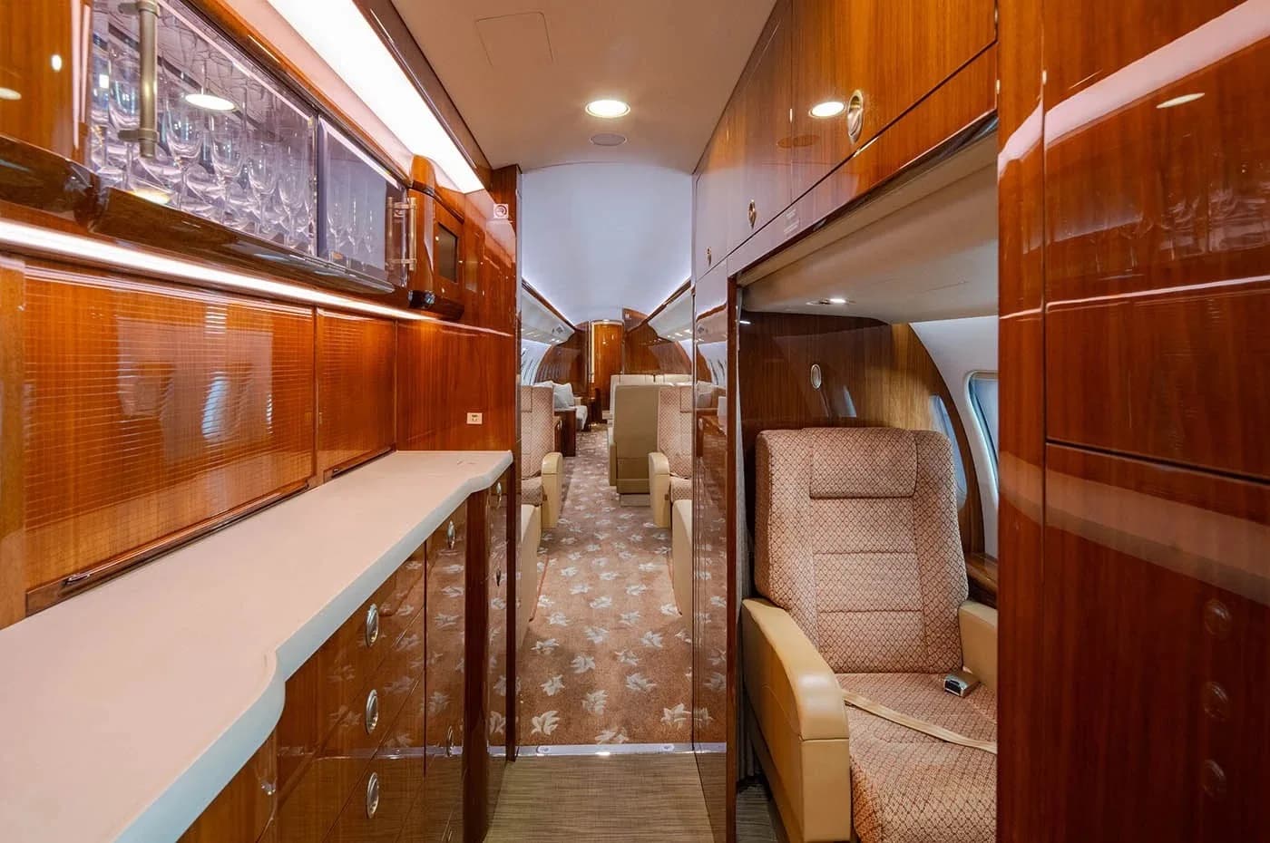 The aircraft galley features polished wood cabinetry and a counter, leading into the main cabin.