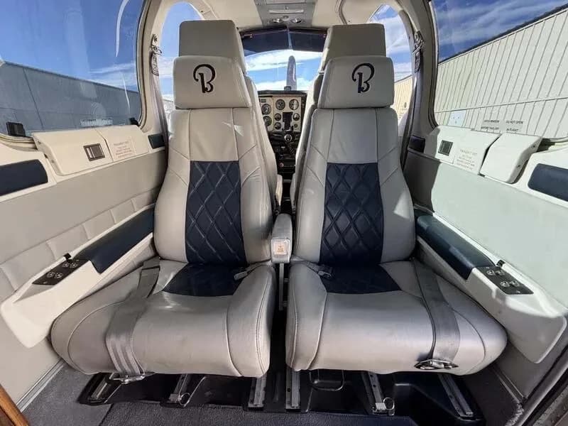 The aircraft's cabin interior with two grey and black quilted seats in the foreground, facing the cockpit.