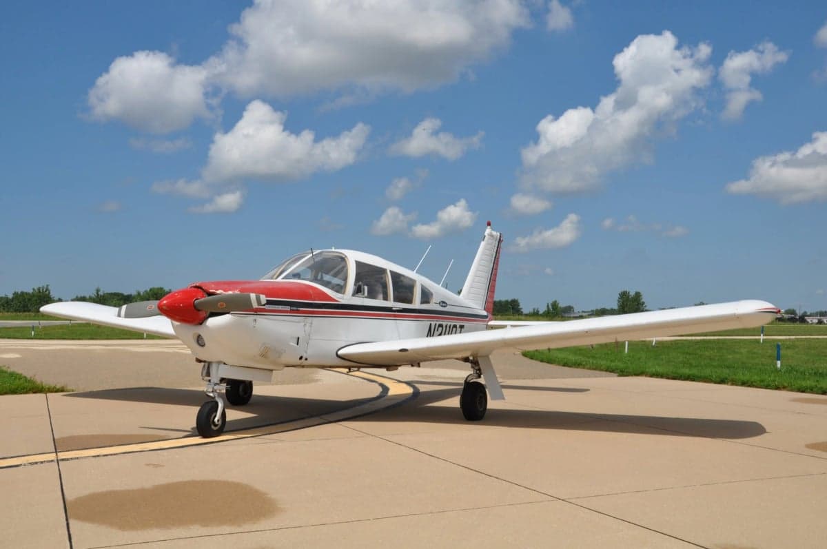 A Piper PA-28 Cherokee is parked on the tarmac on a sunny day.