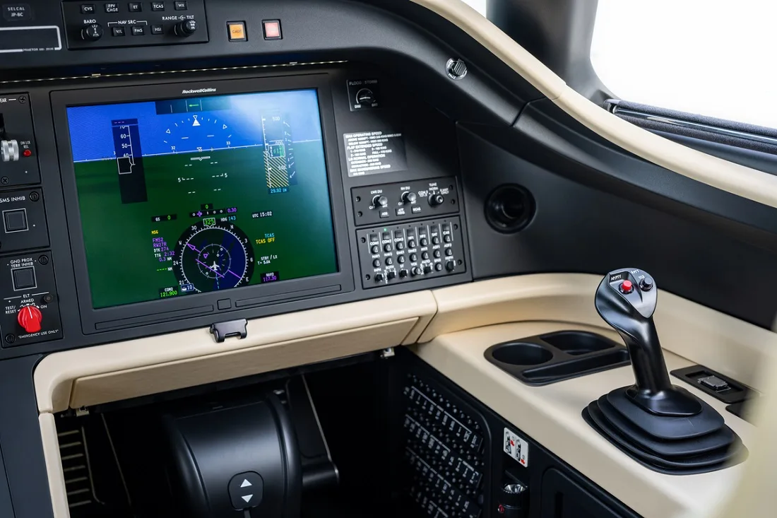 A close-up view of a modern aircraft cockpit with a large primary flight display and side-stick controller.