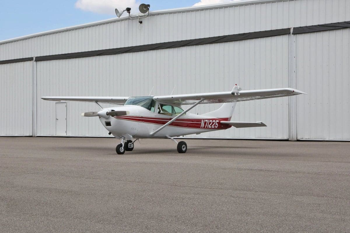 Side view of a Cessna aircraft with a white and red paint scheme parked in front of a hangar, showing the tail number N71225.