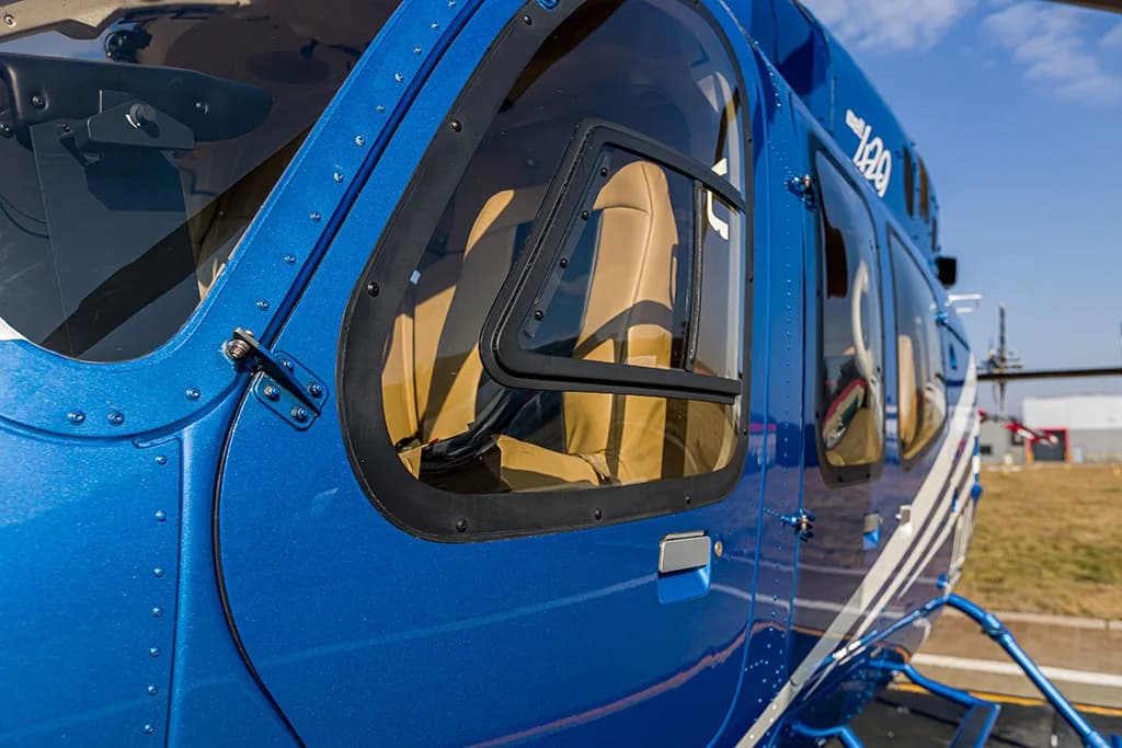 A close-up of the blue helicopter's fuselage, showing a window with tan interior seats visible.