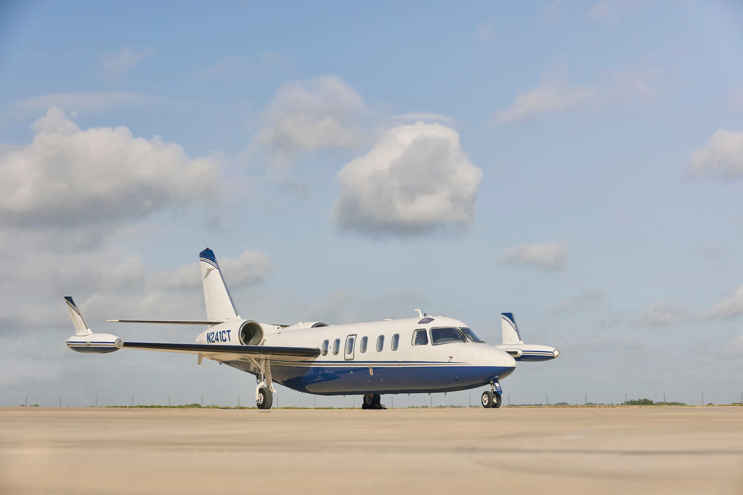 A white and blue jet aircraft sits on the tarmac under a cloudy sky.