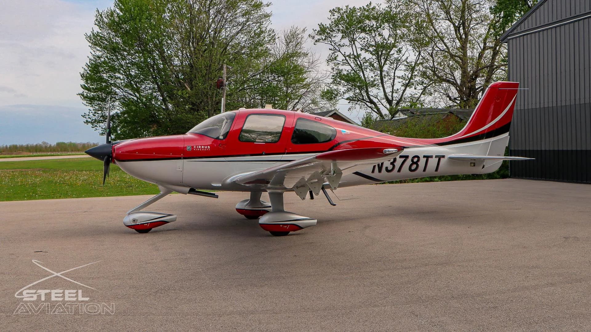 A red and white Cirrus SR22 aircraft with tail number N378TT is shown from the right side, parked on an apron with trees in the background.