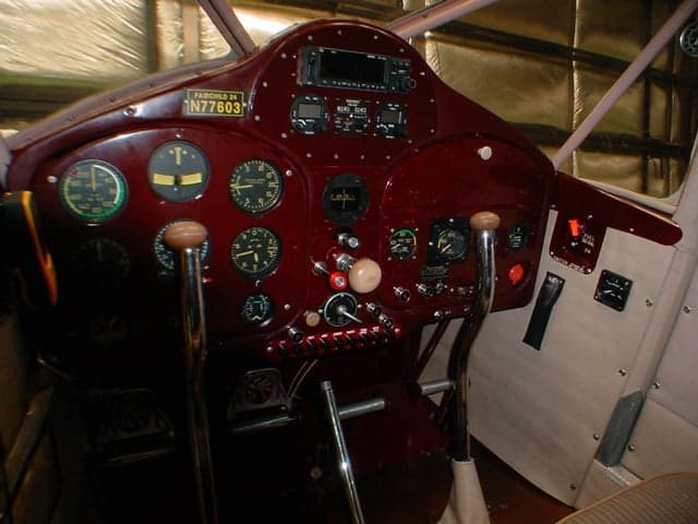 A wider view of the dark red cockpit instrument panel and controls of a Fairchild 24 aircraft.