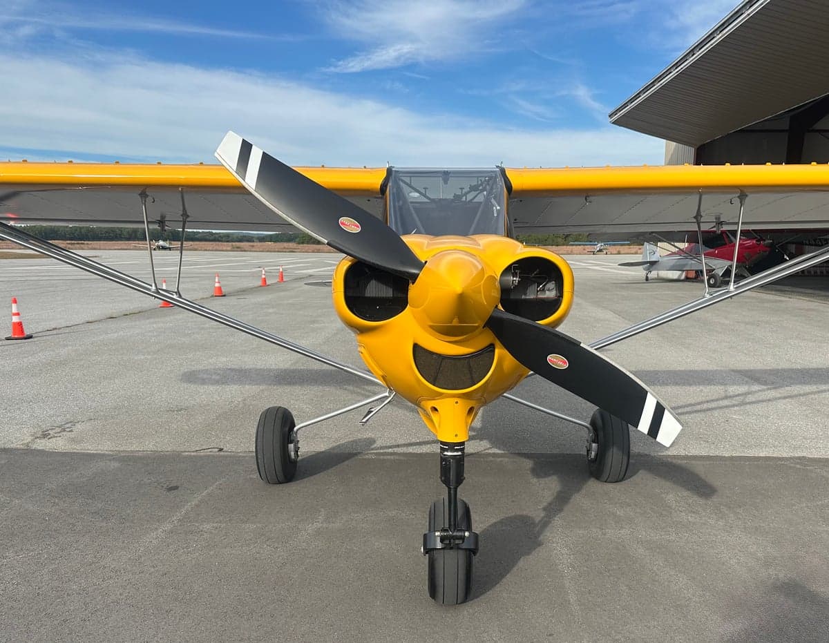 A yellow NX Cub aircraft, N292CC, seen from the front with its propeller, parked on an airfield.