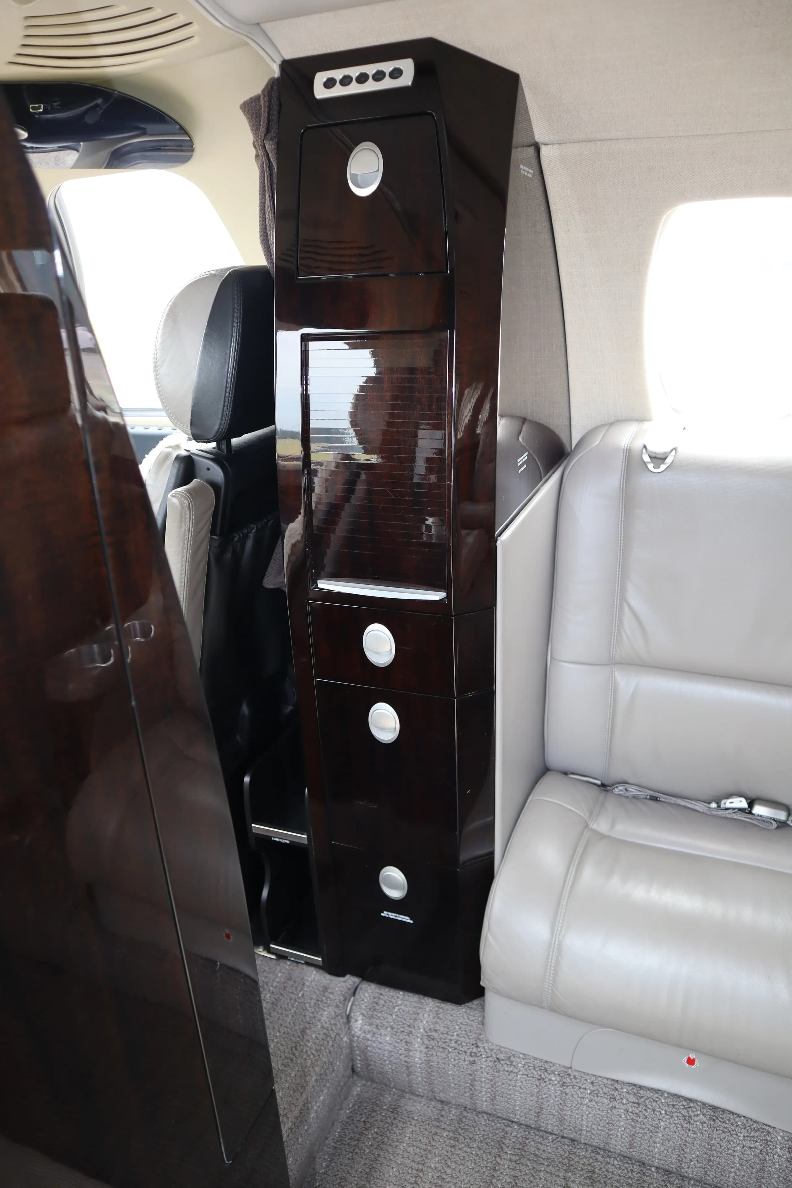 A close-up of a dark wood cabinet with drawers and controls inside the business jet cabin.