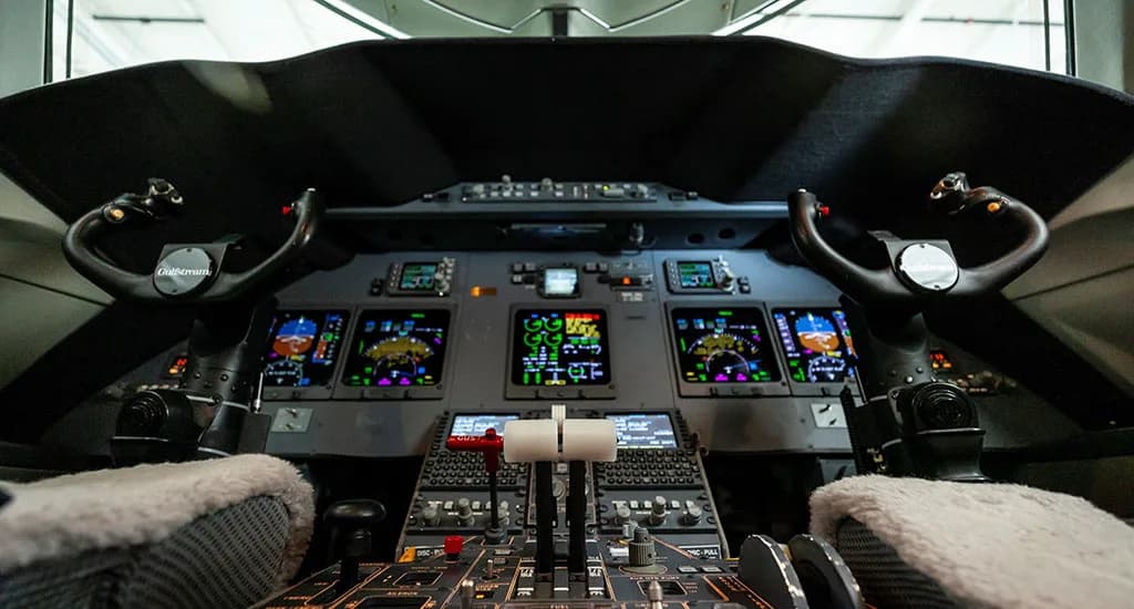 The cockpit of a modern business jet, featuring multiple digital displays, control yokes, and a central throttle quadrant.