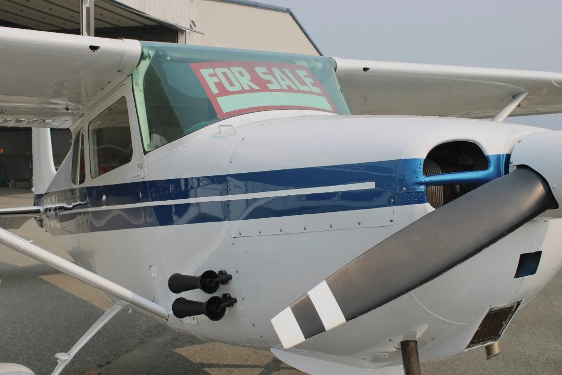 Close up of the front of a Cessna 172 with blue stripe and a 'FOR SALE' sign in the window.