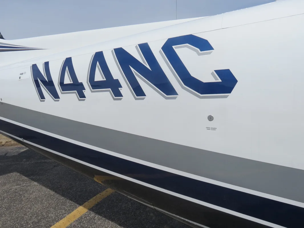 Head-on view of a white twin-engine propeller aircraft with blue and gray stripes parked on an airfield.